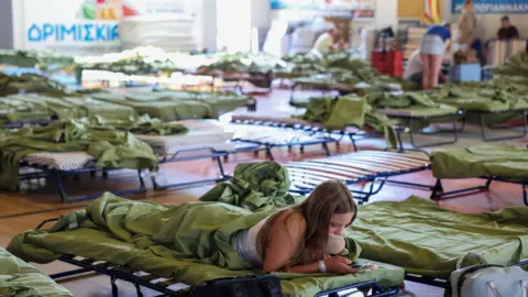 Reuters A tourist takes shelter at the sports hall of the town of Moires as a wildfire burns on the island of Crete,