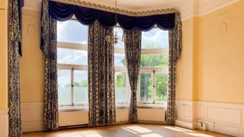 LOWE A high-ceilinged room in an Edwardian home with ornate curtains 