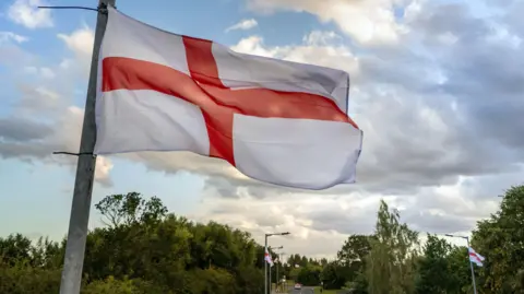 PA Media St George's Cross flags fly from lampposts next to a road.