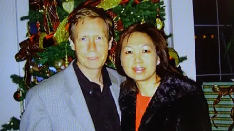 Getty Images A police handout of Peter Chadwick and his wife Quee Choo Chadwick. They are shoulder to shoulder and looking at the camera, stood in front of a Christmas tree. He is in a grey suit jacket and black shirt, she is wearing a red top and black jacket.