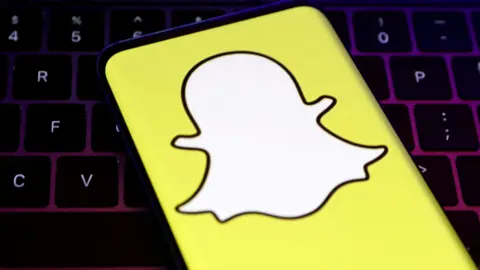 Reuters A closeup of Snapchat's logo, a white cartoon ghost with a bright yellow background, held over a laptop conputer keyboard.