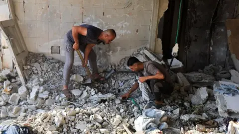 Reuters Two men search through rubble 