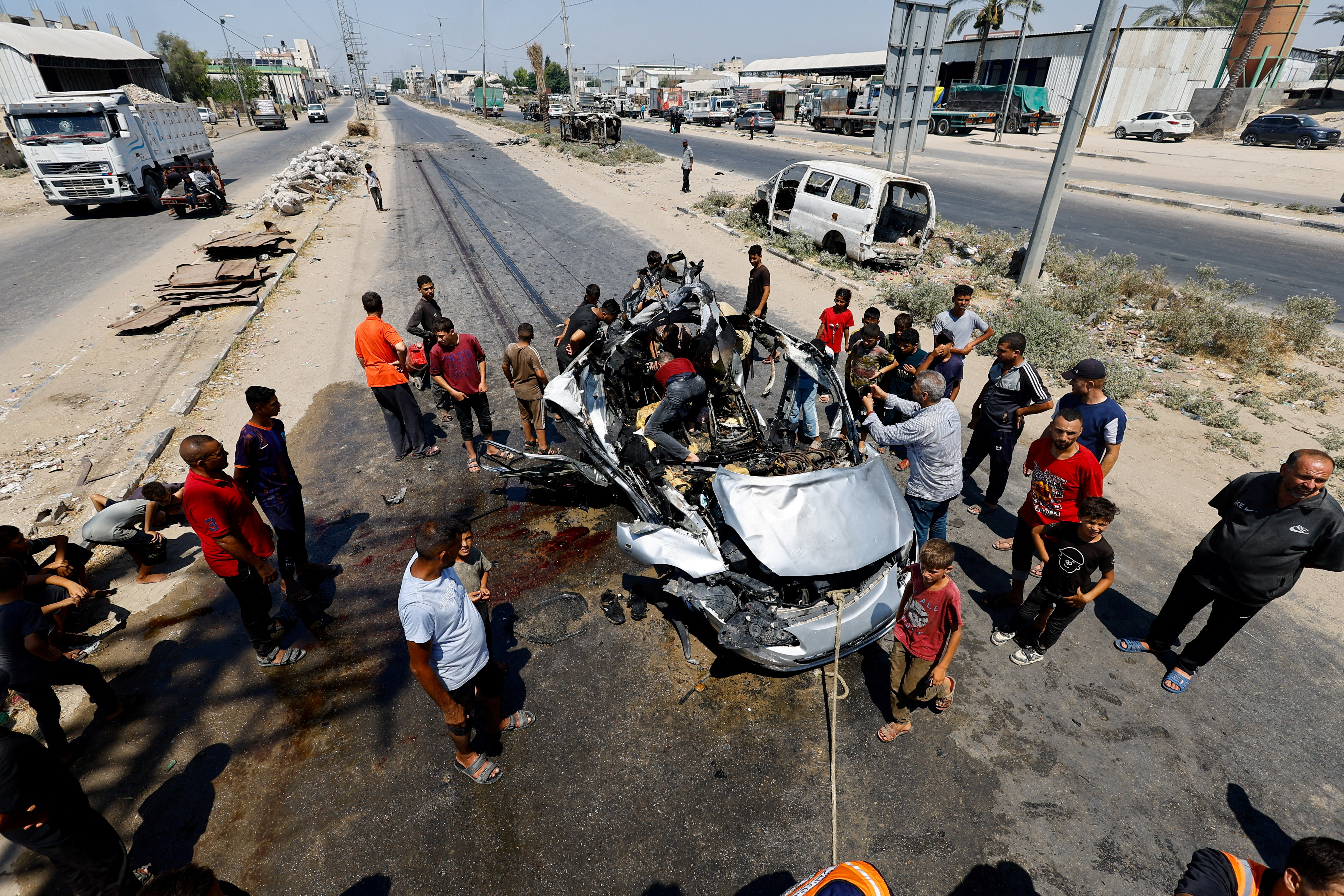 Palestinians inspect the site of an Israeli strike on a vehicle, in Deir al-Balah