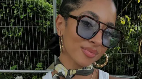 Chelsea Boyce A woman is wearing large sunglasses and earrings, and is looking at the camera.