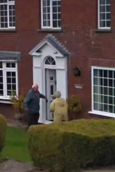 Google A man and a woman are stood outside a large red-brick home. He is holding the door open for her in the dooway.