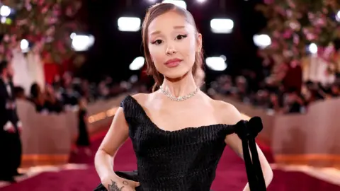 Getty Images Ariana Grande appears on a red carpet in January wearing a black dress.