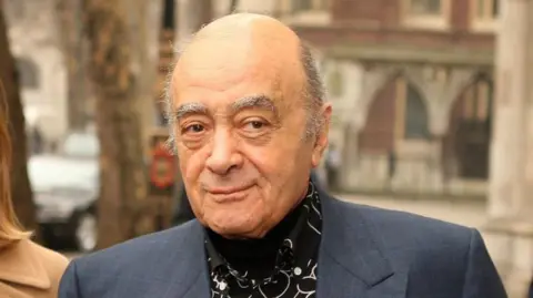 Getty Images Harrods owner Mohamed Al Fayed wearing a suit and black shirt