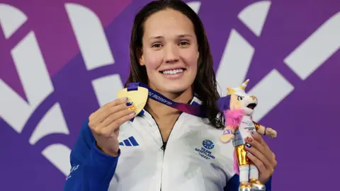 Getty Images Angharad Evans smiling on the podium, holding her gold medal and a little toy mascot.