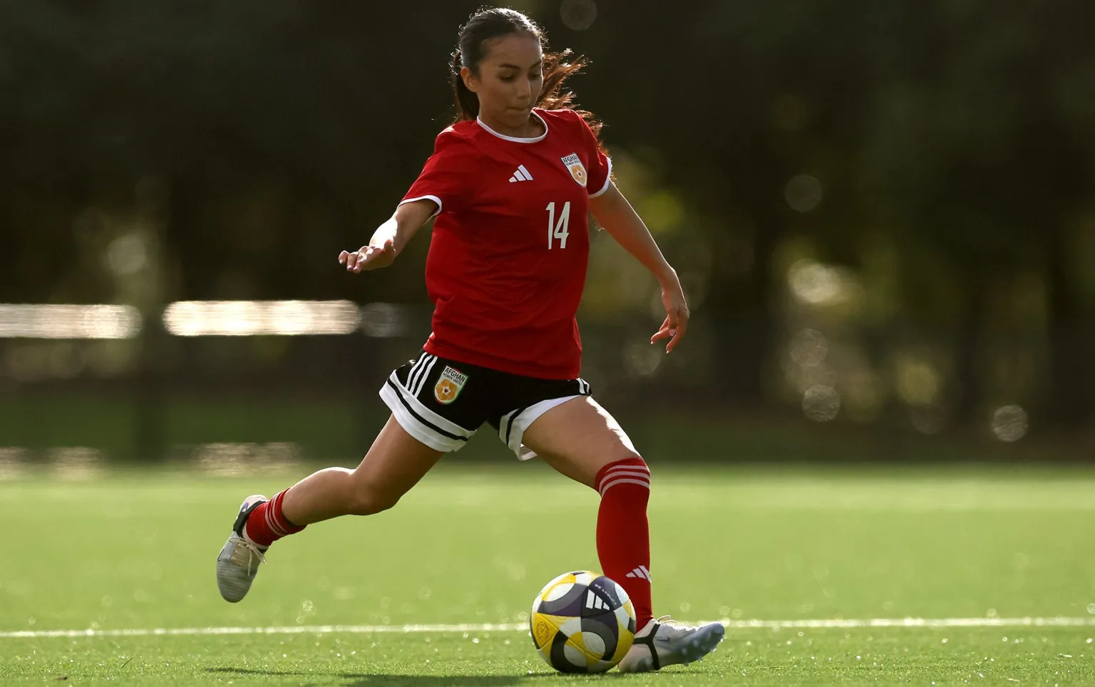 Phil Walter/Getty Images Action shot of a woman about to kick a football. She is wearing a red shirt with the number 14 on it in white. She has black shorts, red socks and white boots. Her long dark hair is tied in a ponytail.